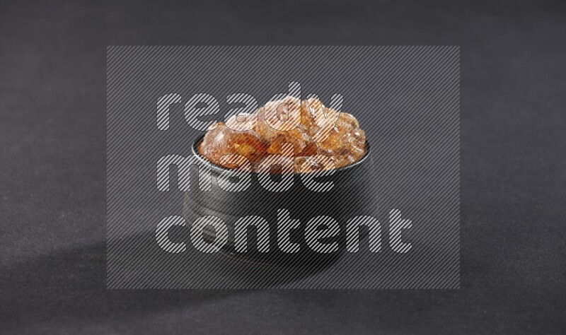A black pottery bowl full of gum arabic on black flooring