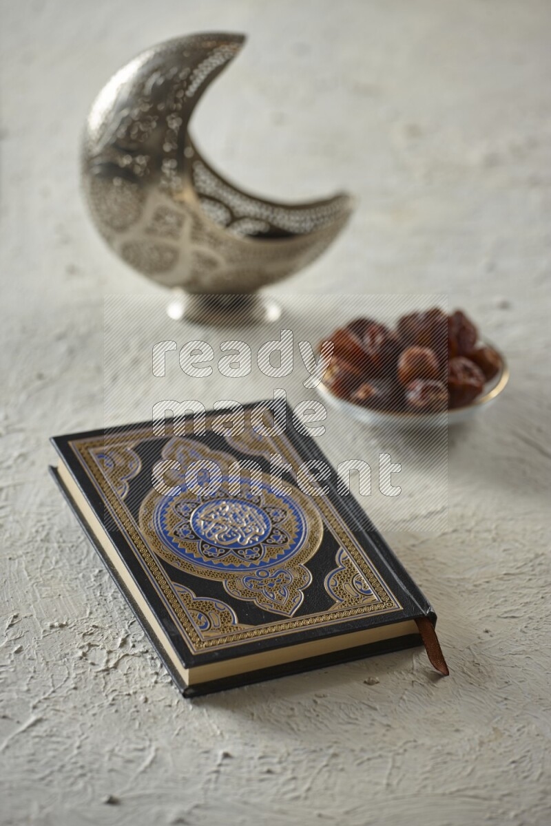 A silver lantern with different drinks, dates, nuts, prayer beads and quran on textured white background