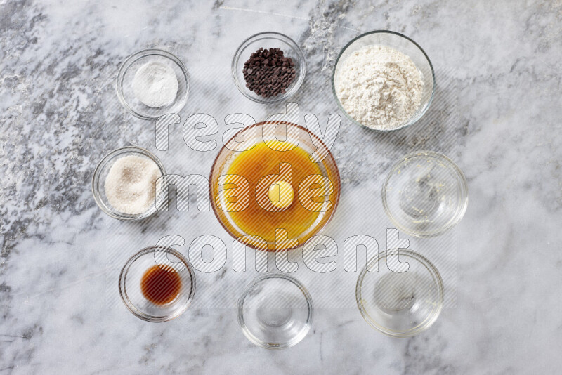 Cookies step by step with its ingredient, flour, butter, brown sugar, egg, vanilla extract, white sugar, chocolate chips and baking soda on grey marble background