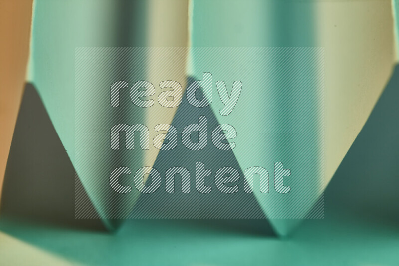 A close-up abstract image showing sharp geometric paper folds in green gradients and warm tones