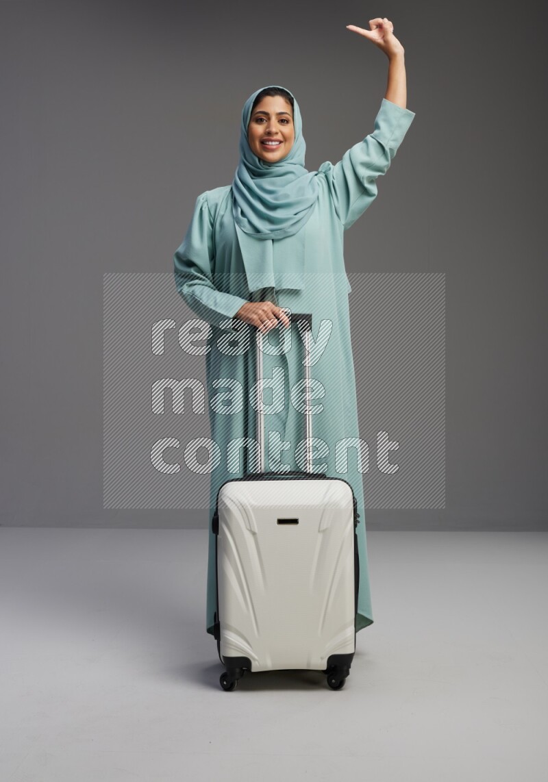 Saudi Woman wearing Abaya standing holding Travel bag on Gray background
