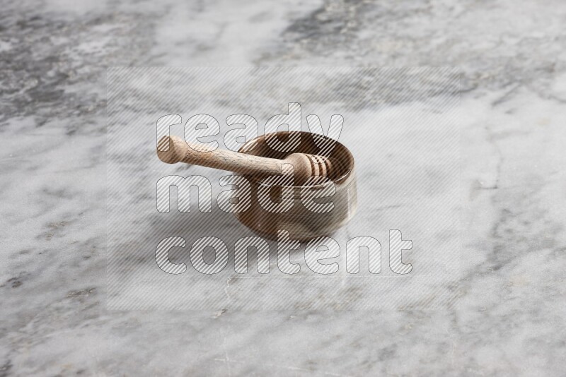 Brown pottery bowl with wooden honey dipper in it on grey marble background