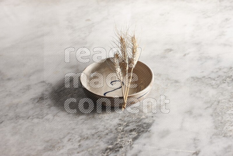 Wheat stalks on multicolored pottery bowl on grey marble background