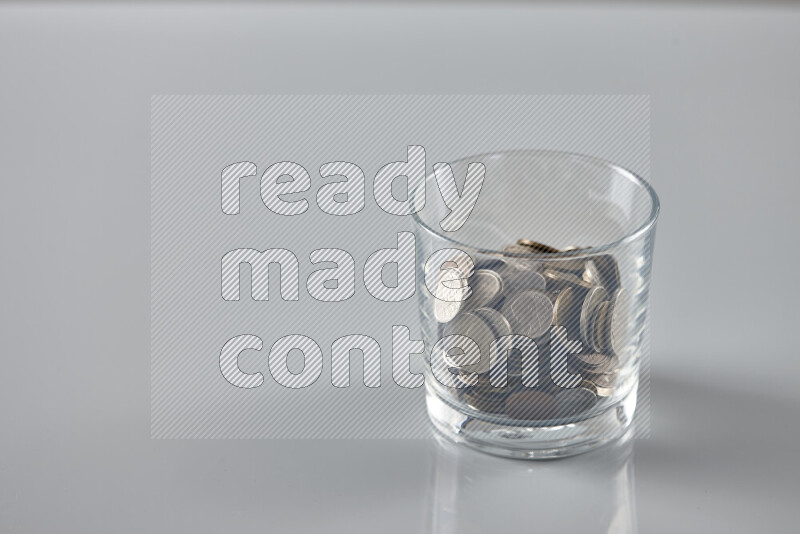 Random old coins in a glass cup on grey background