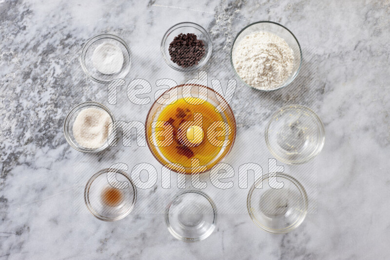 Cookies step by step with its ingredient, flour, butter, brown sugar, egg, vanilla extract, white sugar, chocolate chips and baking soda on grey marble background