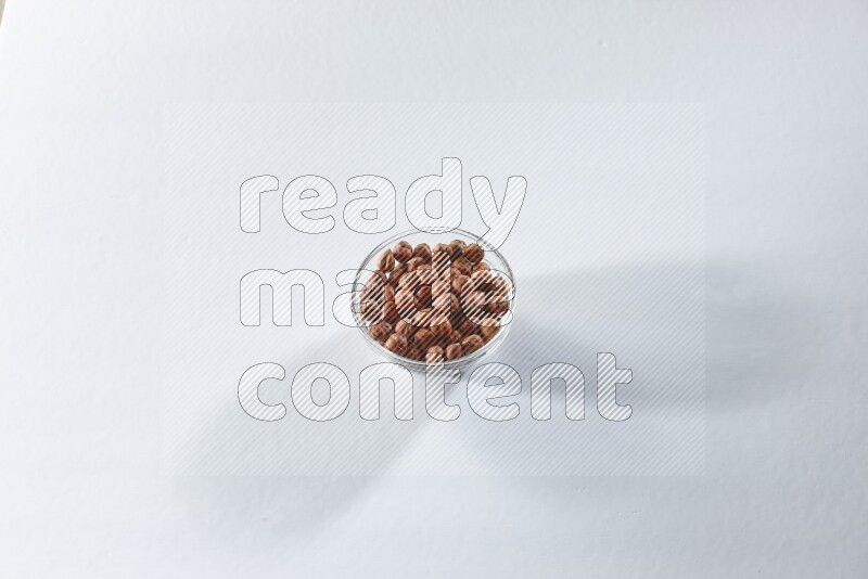 A glass bowl full of peeled hazelnuts on a white background in different angles