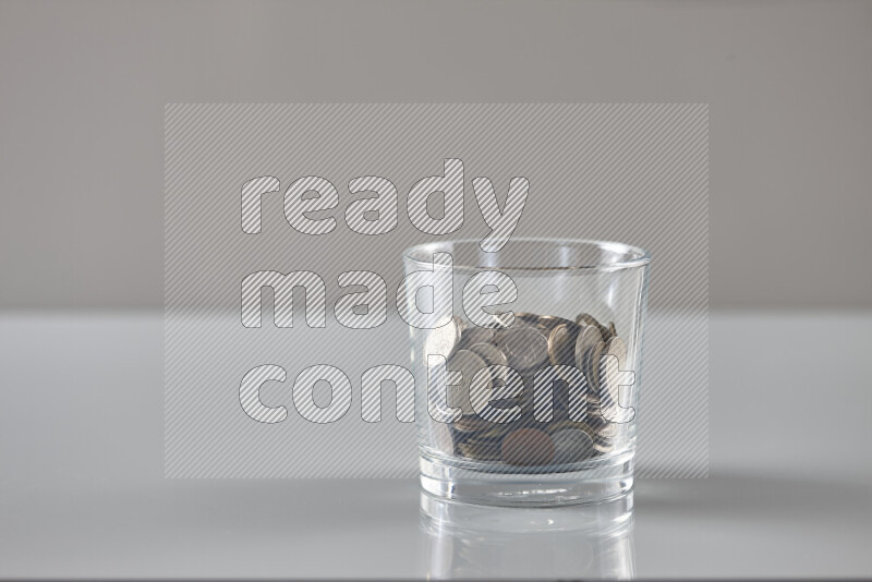 Random old coins in a glass cup on grey background