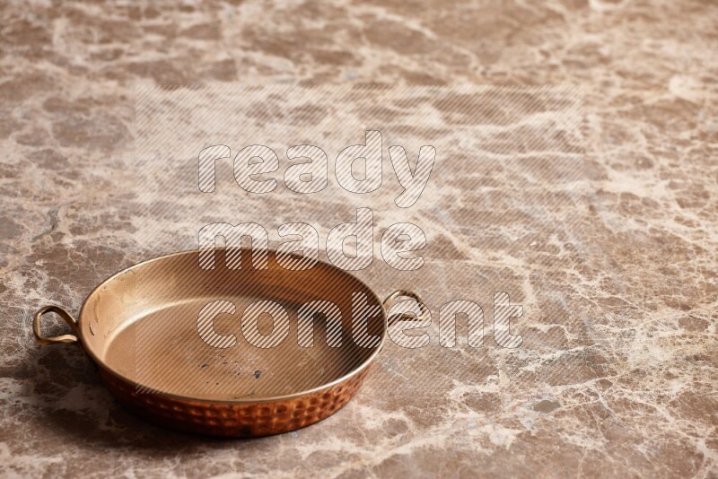 A small copper pan on beige marble background