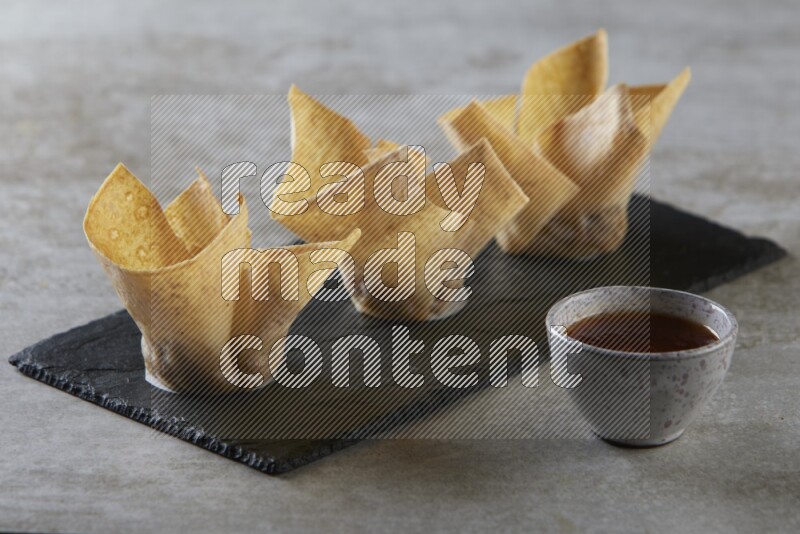 wonton cups with soy sauce ramkin on rectangle slate on grey textured counter top