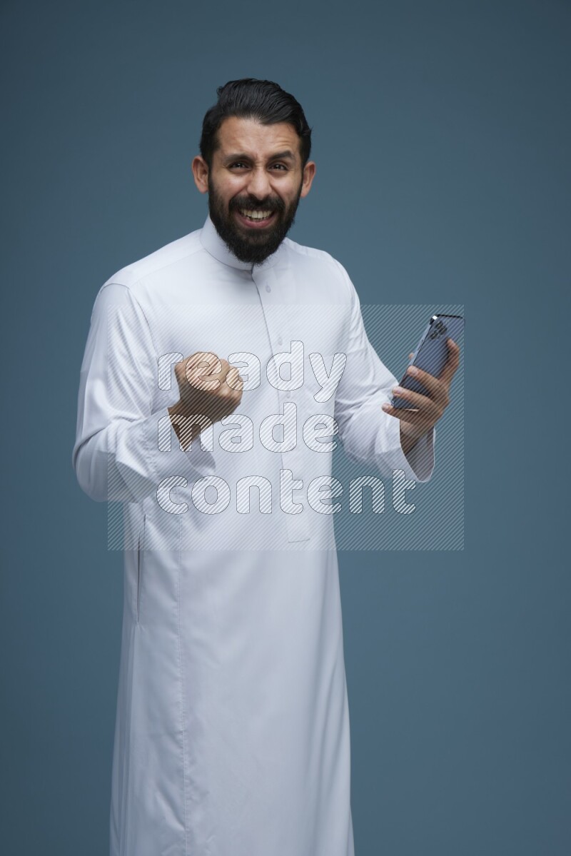 A man Texting in a blue background wearing Saudi Thob