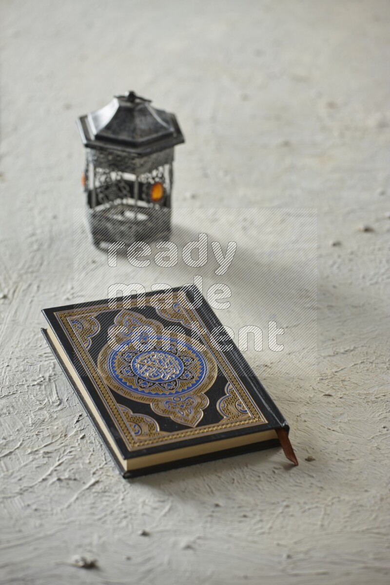 A silver lantern with different drinks, dates, nuts, prayer beads and quran on textured white background