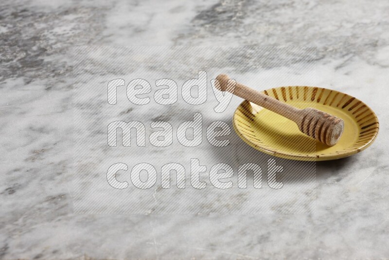 Multicolored pottery plate with wooden honey dipper in it on grey marble background