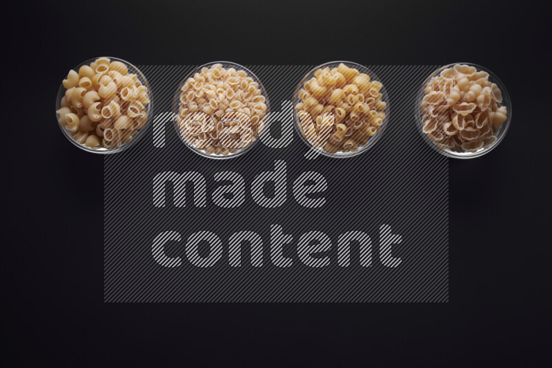 Different pasta types in glass bowls on black background