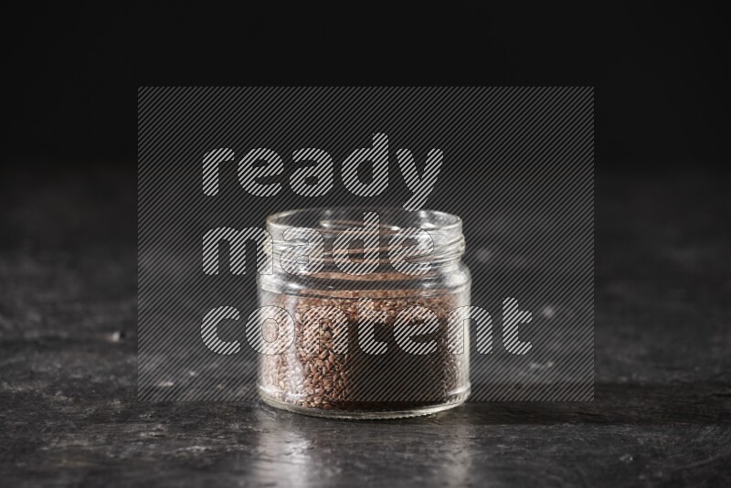 A glass jar full of flaxseeds on a textured black flooring