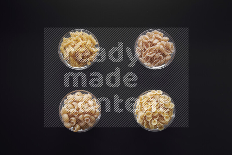 Different pasta types in glass bowls on black background