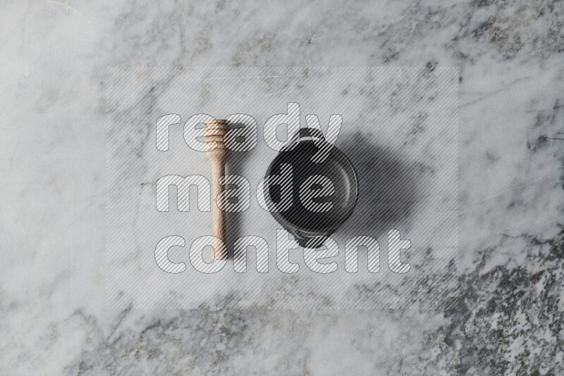 Black pottery bowl with wooden honey dipper on the side on grey marble background