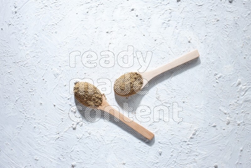 Wooden spoons full of allspice powder and allspice whole balls spreaded on a textured white flooring