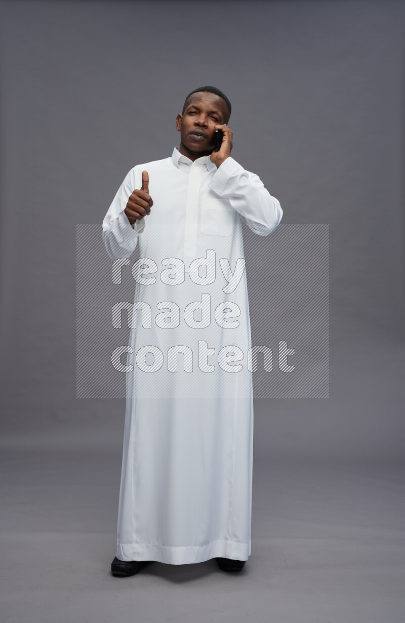 Saudi man wearing thob standing talking on phone on gray background