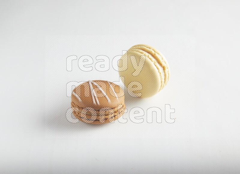 45º Shot of of two assorted Brown Irish Cream, and Yellow Vanilla macarons on white background