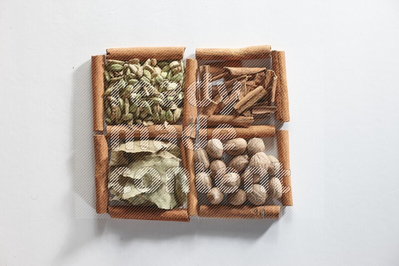 4 مربعات من أعواد القرفة ممتلئة بجوزة الطيب وأوراق الغار وحبوب الهيل والقرفة على أرضية بيضاء