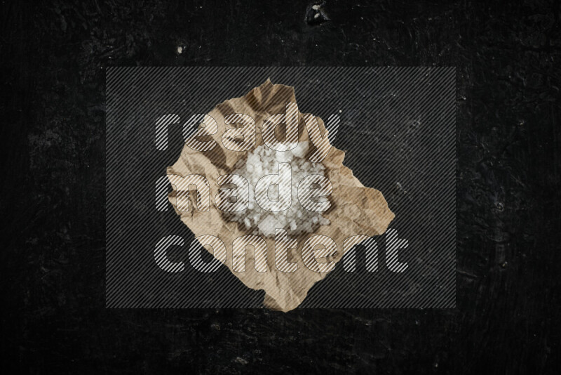 A crumpled piece of paper full of white salt on black background