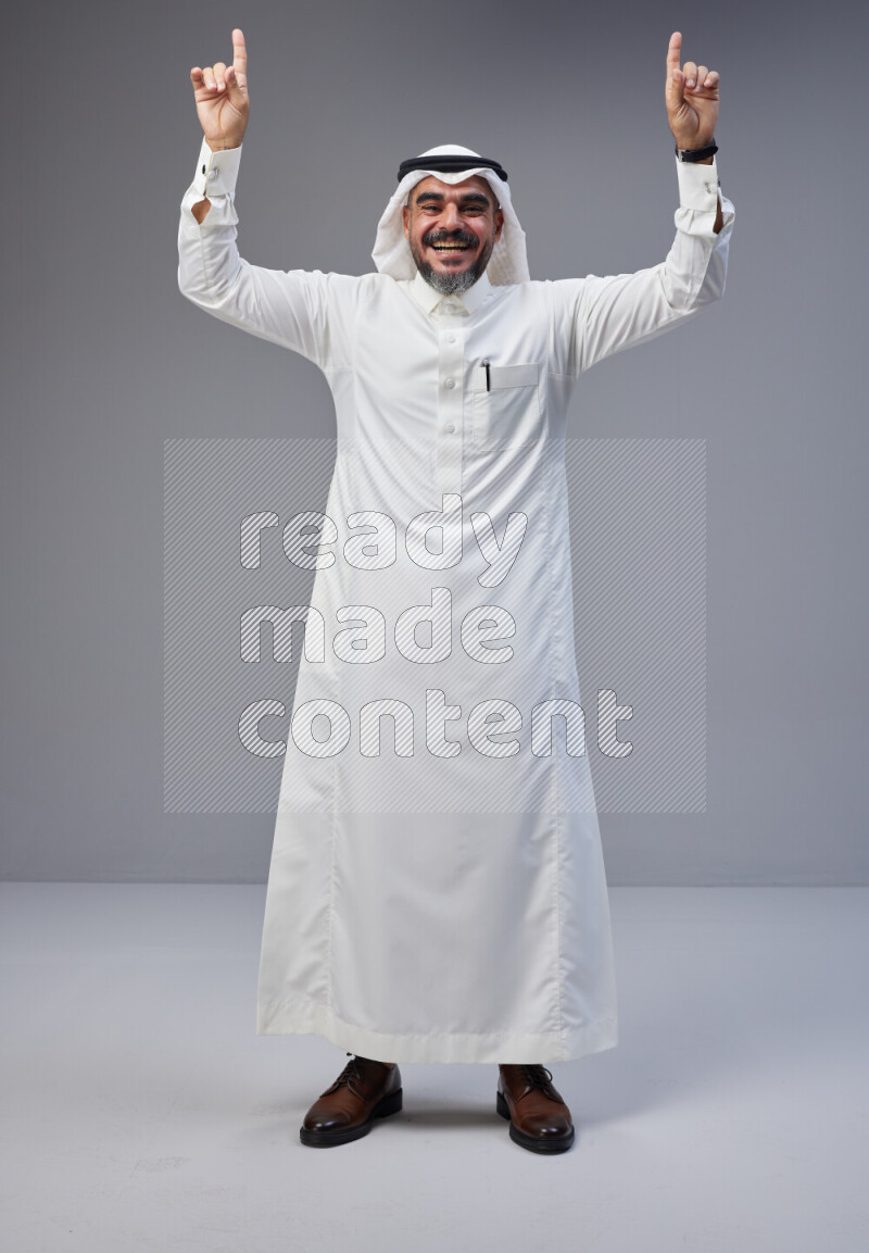 Saudi man Wearing Thob and white Shomag standing interacting with the camera on Gray background