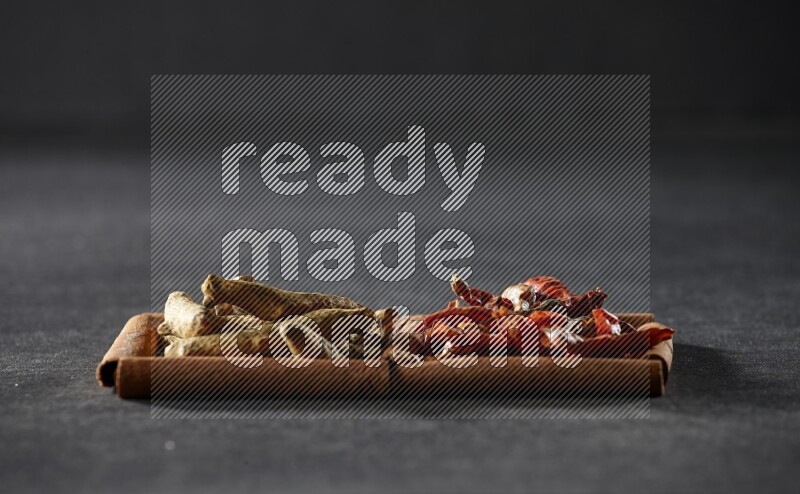 2 squares of cinnamon sticks full of chilis and turmeric fingers on black flooring