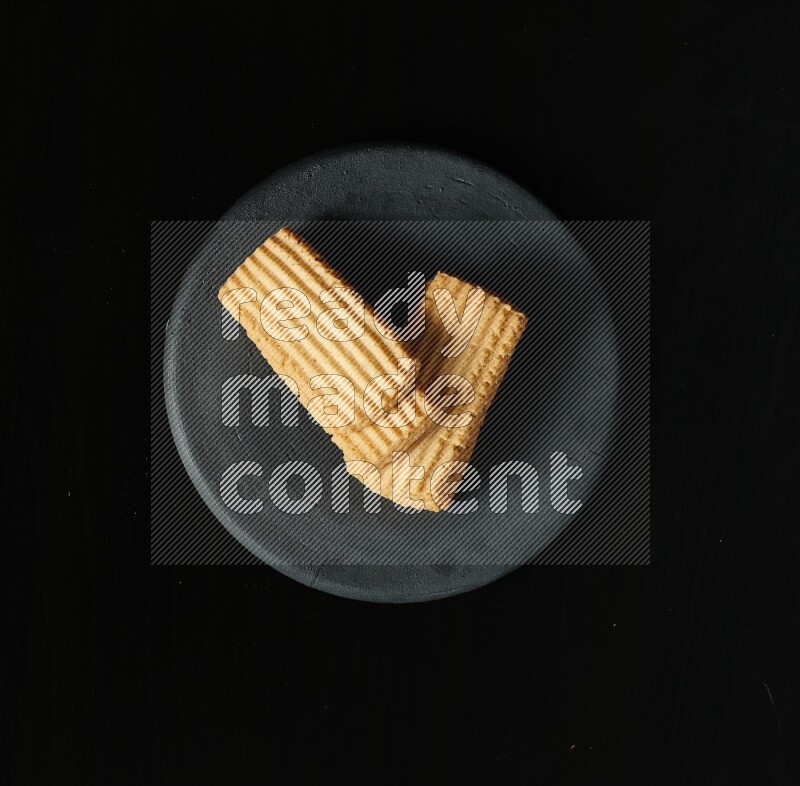 Golden biscuits in a black pottery plate on black background
