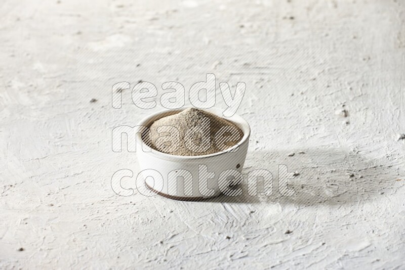 white pottery bowl full of white pepper powder on textured white flooring