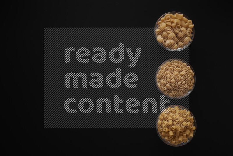 Different pasta types in 3 glass bowls on black background