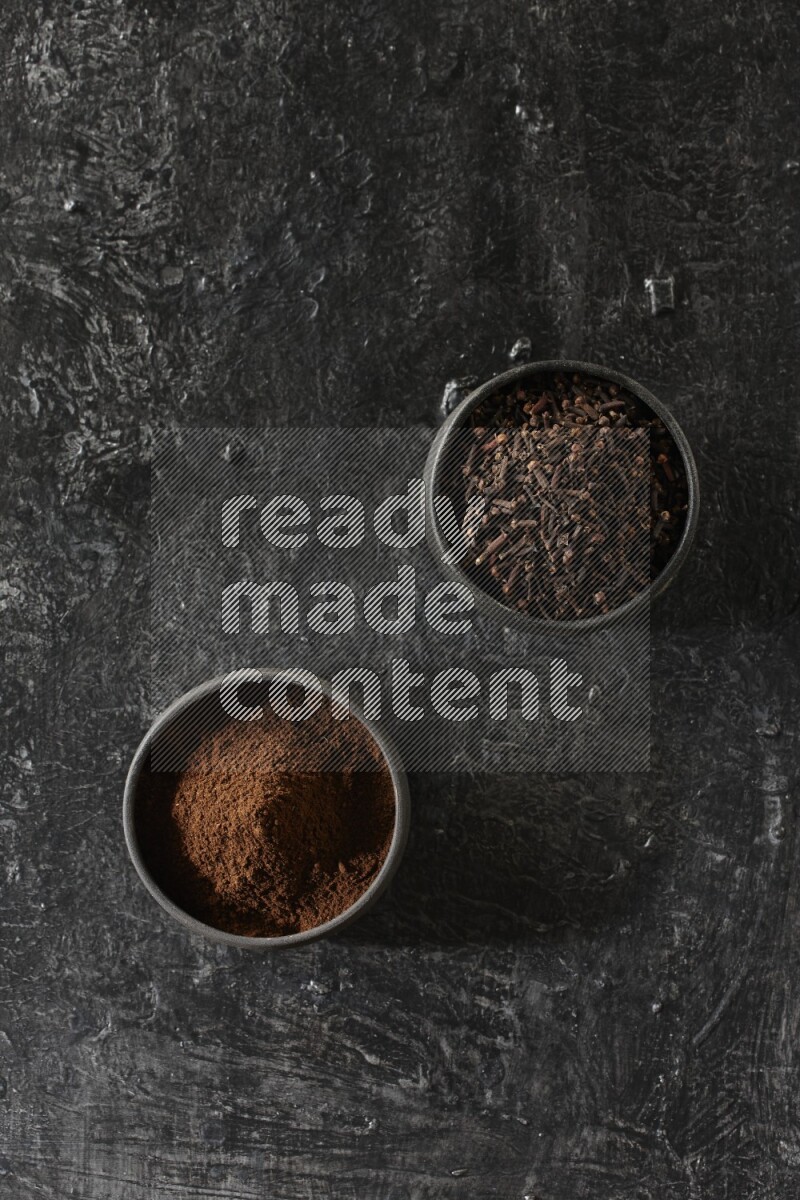 وعاءين من الفخار الأسود أحدهما ممتلئي بحبوب القرنفل والآخر ممتلئ ببودرة القرنفل على خلفية سوداء