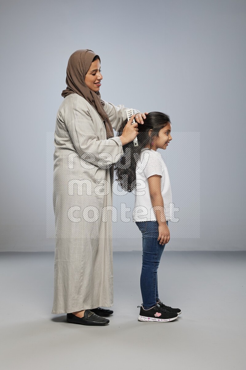 Mom standing styling hair for her daughter on gray background