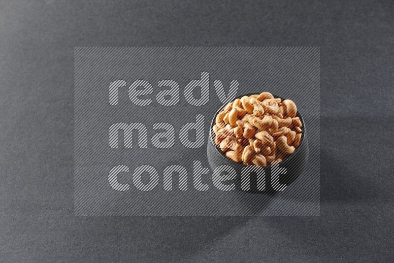 A black pottery bowl full of cashews on a black background in different angles