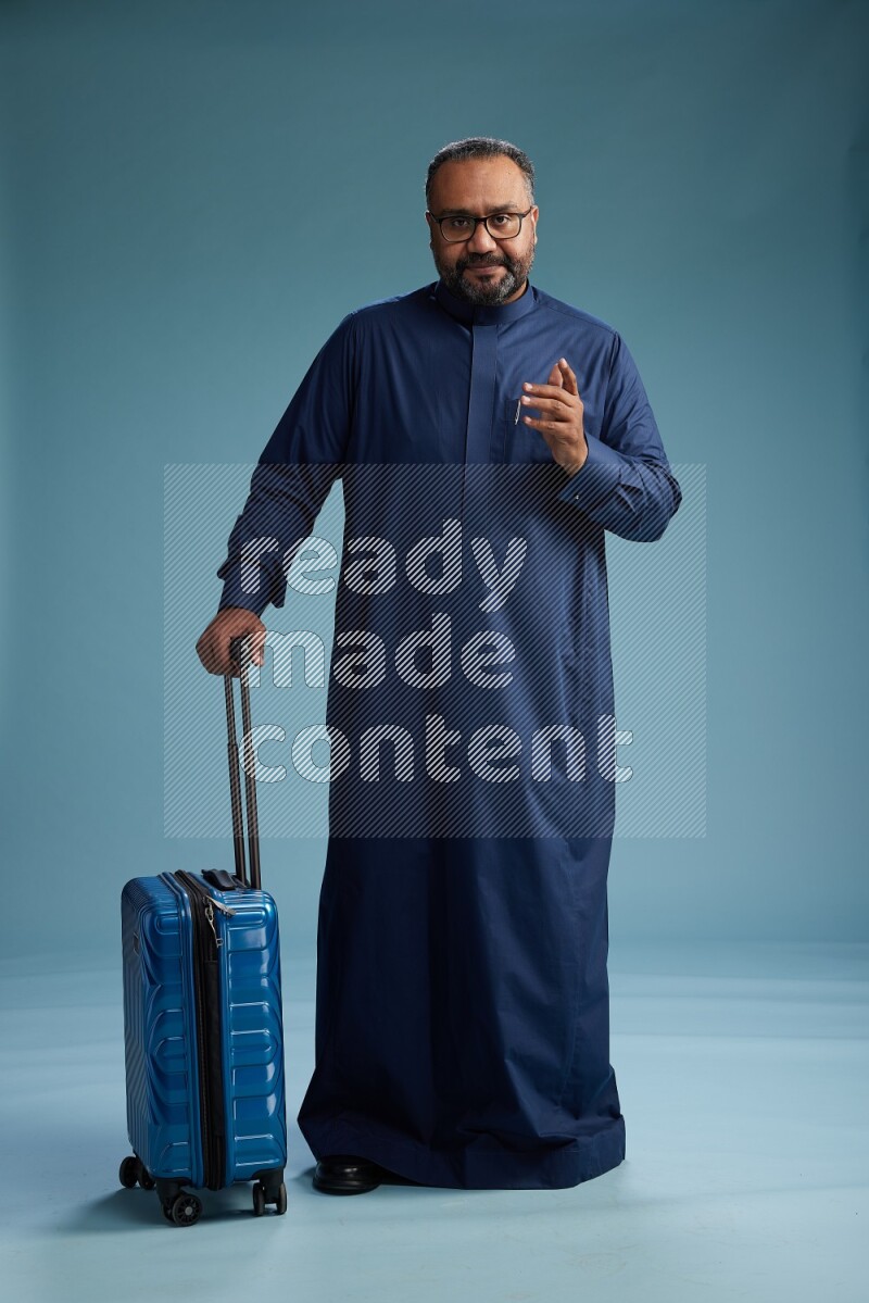 Saudi Man without shimag Standing pulling travel bag on blue background