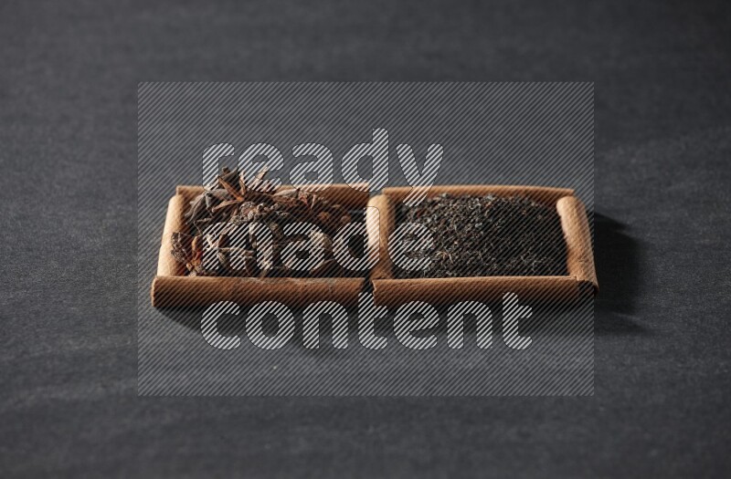 مربعان من أعواد القرفة ممتلئان باليانسون النجمي والشاي الأسود علي خلفية سوداء