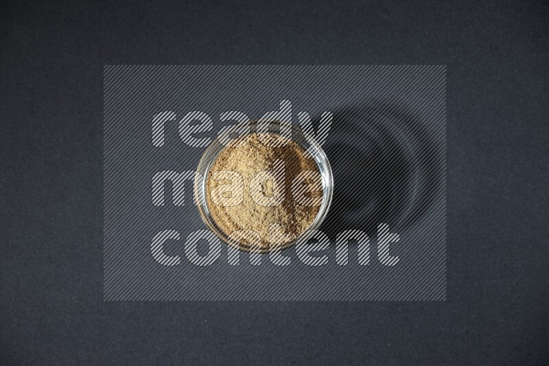 وعاء زجاجي ممتلئ ببودرة الكمون على خلفية سوداء