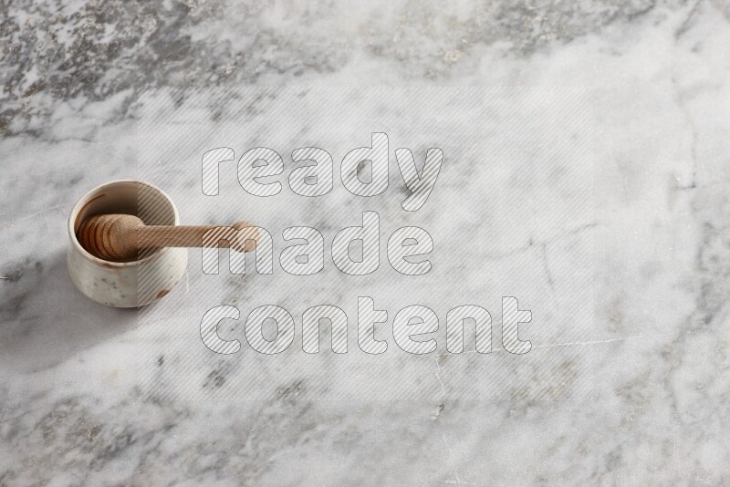 Beige pottery bowl with wooden honey dipper in it on grey marble background