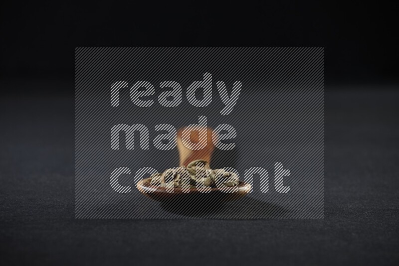 A wooden ladle full of cardamom on black flooring