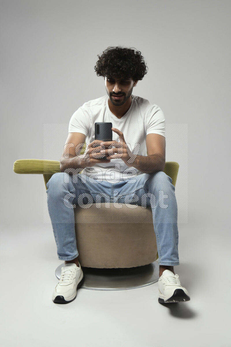 A man wearing casual sitting on a chair shooting with his phone on white background