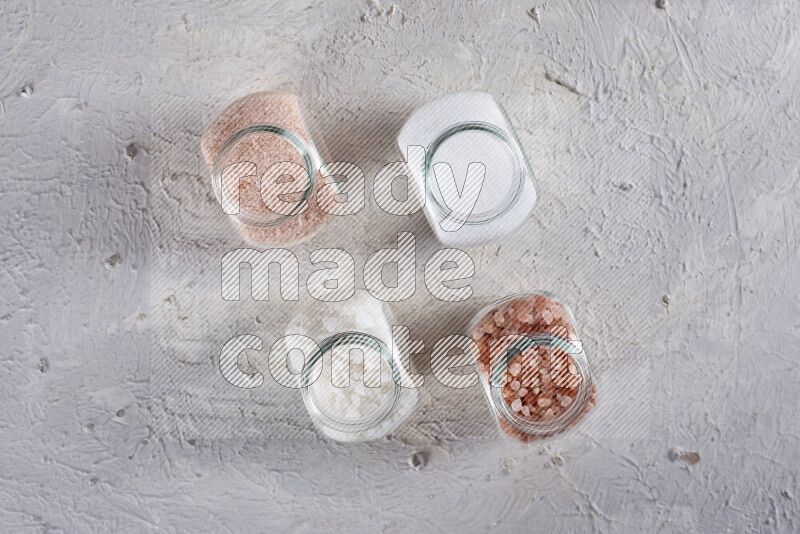 4 glass jars filled with table salt, coarse sea salt, fine himalayan salt and coarse himalayan salt on white background