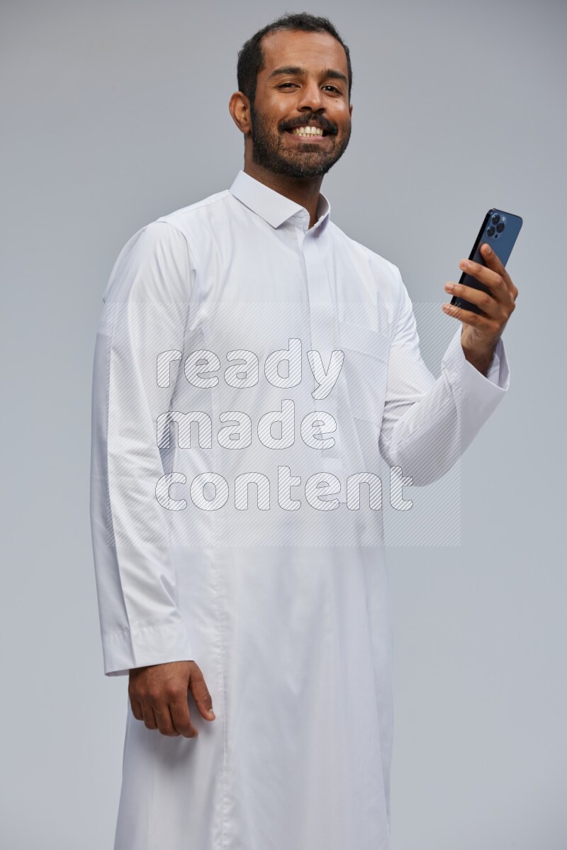 Saudi man wearing Thob standing texting on phone on Gray background