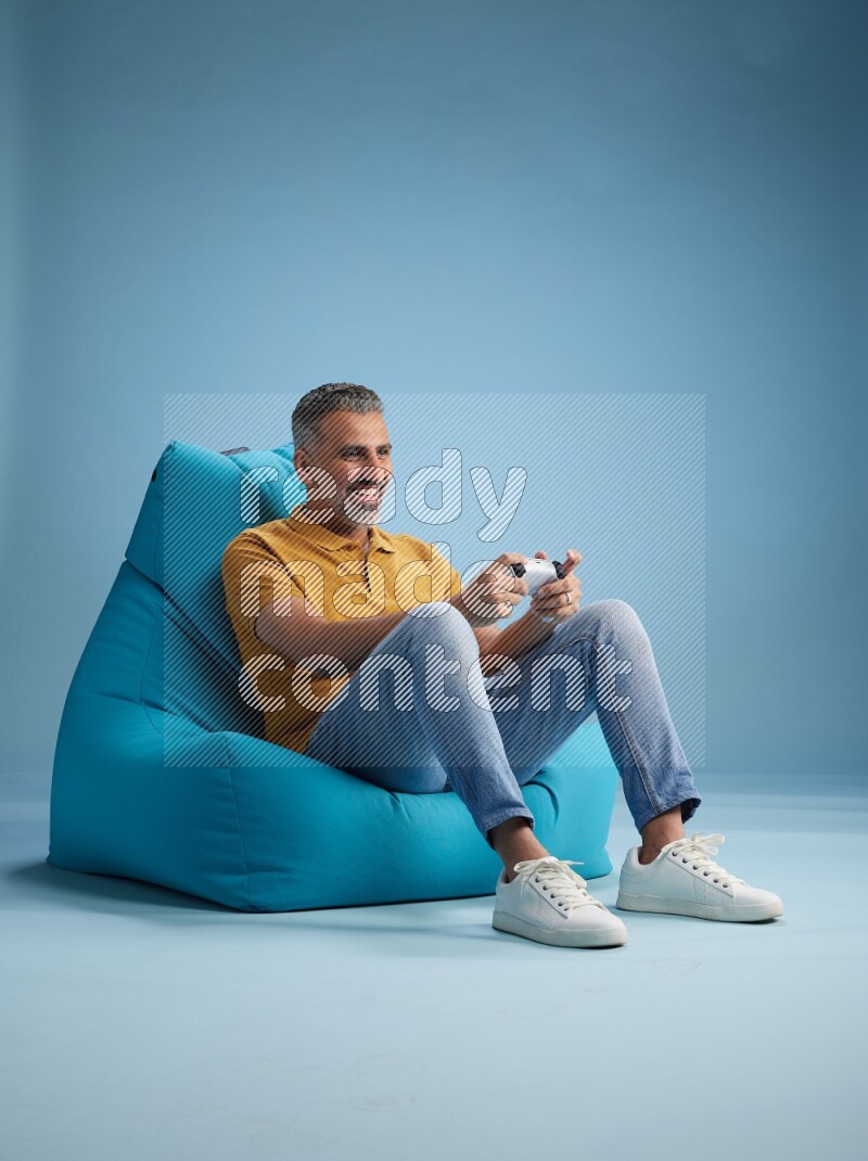 A man sitting on a blue beanbag and gaming with joystick