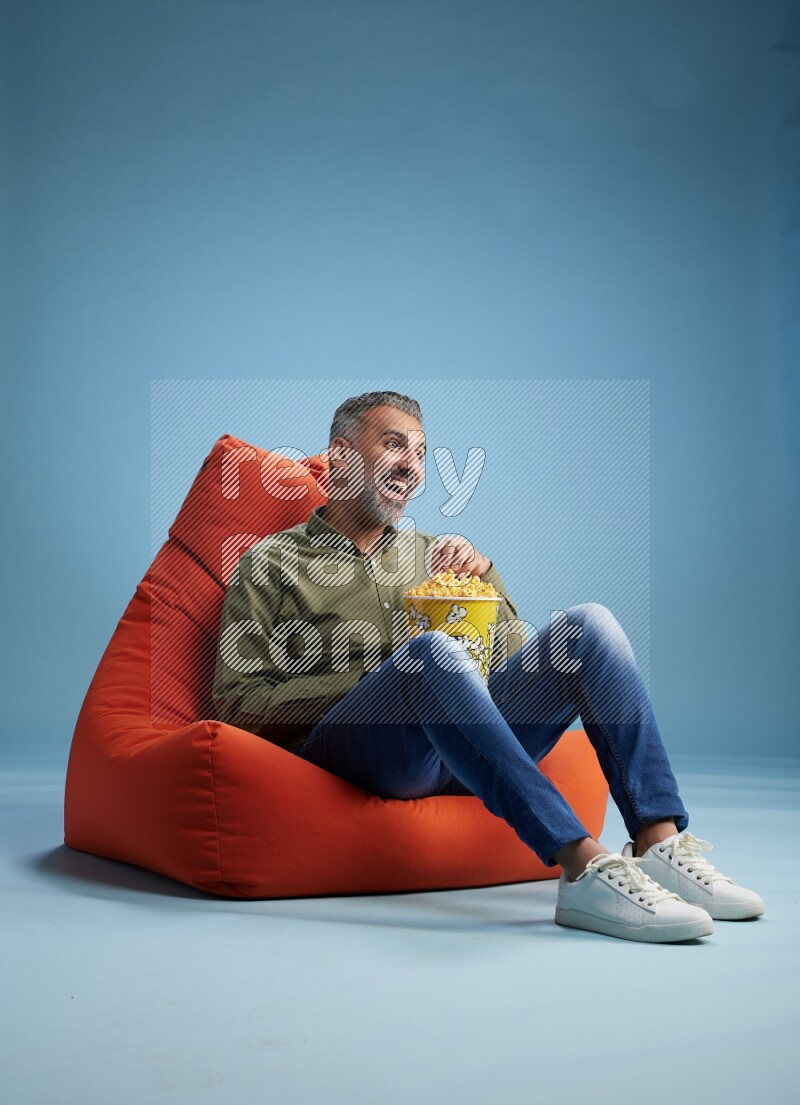 A man sitting on an orange beanbag and eating popcorn