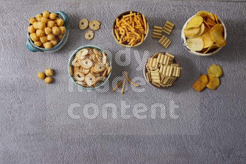 Assorted snacks in pottery bowls on grey background