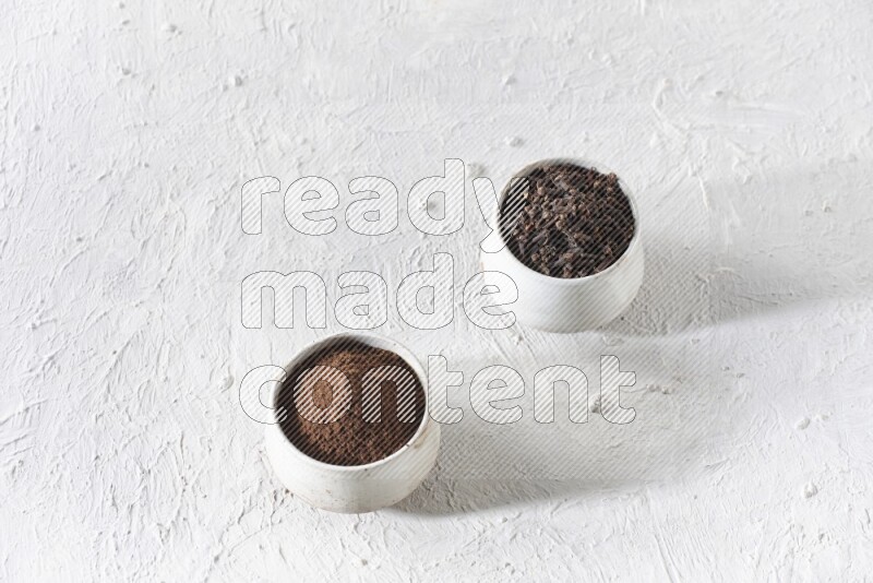 2 Beige ceramic bowls, one full of cloves and the other full of powder on textured white flooring