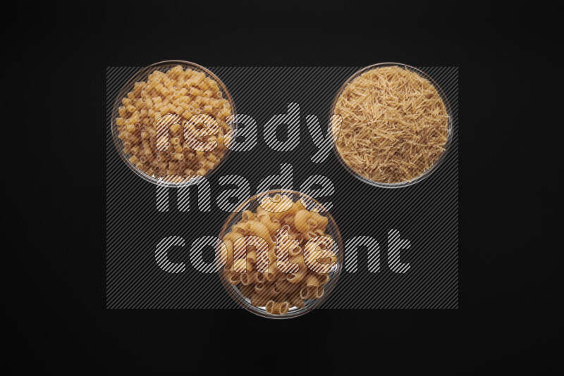 Different pasta types in glass bowls on black background