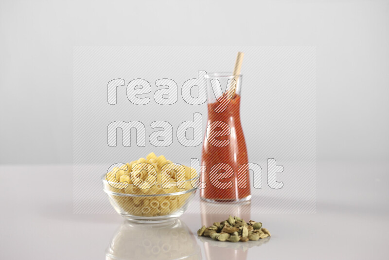 Raw pasta with tomatoe pasta with different ingredients such as cherry tomatoes, basil, garlic, bay laurel, cardamom, white pepper, black pepper, red chilis and wheat stalks on light grey background
