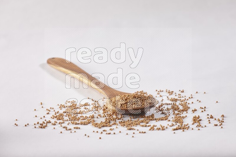 A wooden ladle full of mustard seeds on a white flooring