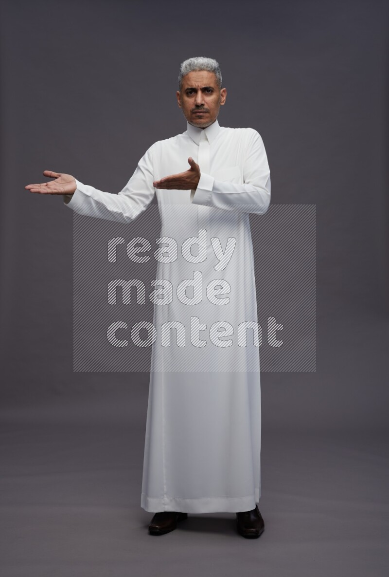 Saudi man wearing thob standing interacting with the camera on gray background