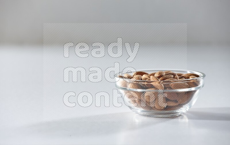 A glass bowl full of peeled almonds on a white background in different angles